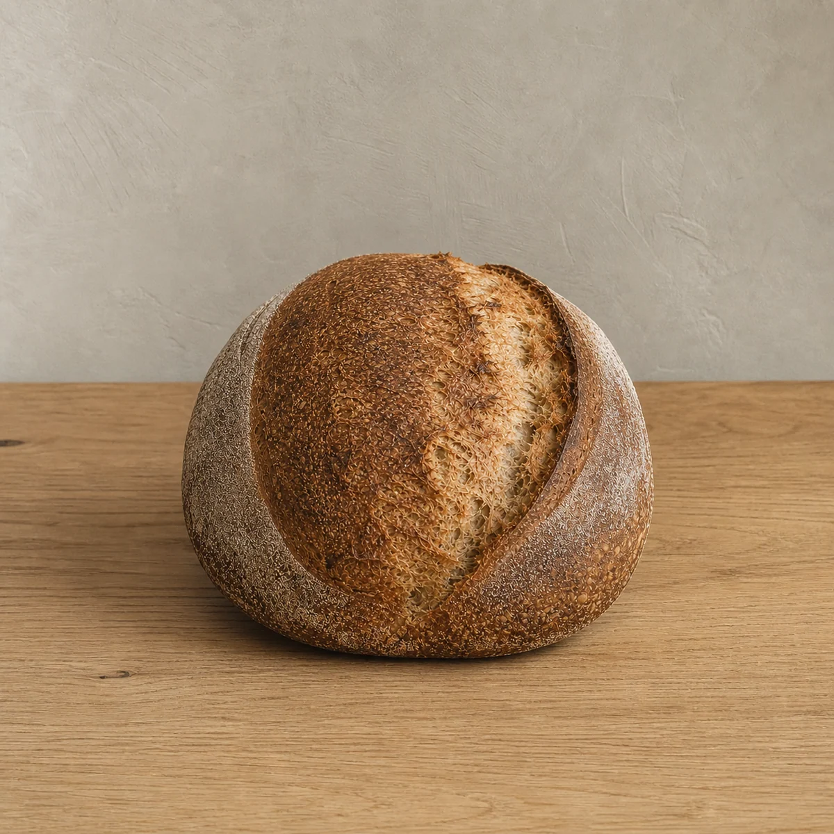 Rond halfvolkoren zuurdesembrood met natuurlijke insnede op een lichte houten werkbank
